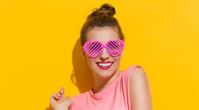 a women in pink heart-shaped sunglasses and pink vest against a bright yellow background