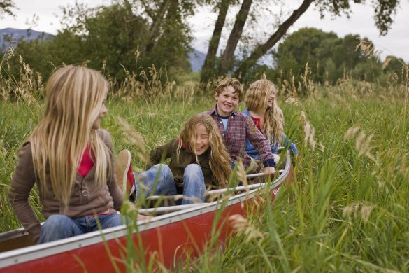 Kids playing in a canoe in a field.